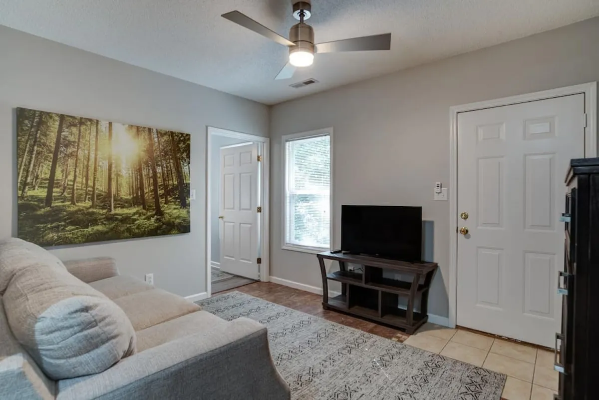A bright, sunlit living room featuring a modern sofa, wall art, and a television. The space exudes a sense of comfort and togetherness, encouraging shared moments and relaxation.