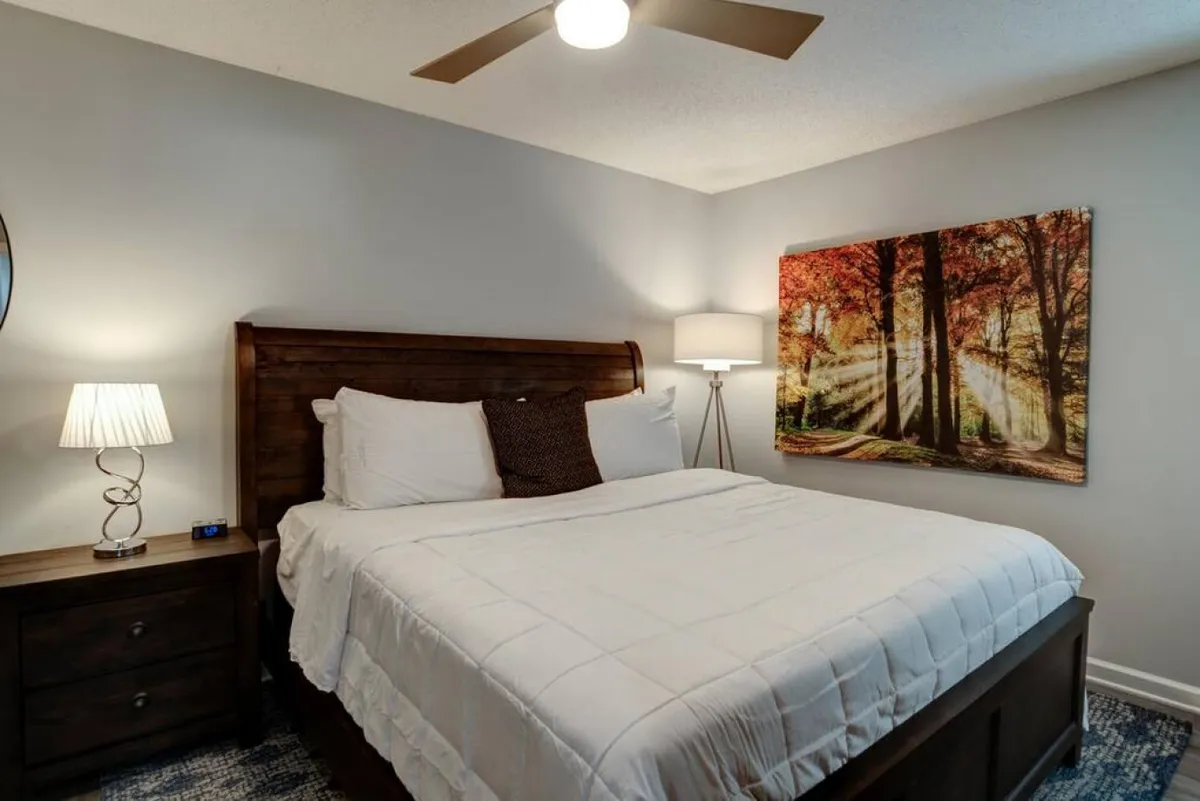 A cozy and serene bedroom scene with a comfortable bed, stylish wall art, a bedside lamp, and a nightstand. The soft lighting and calming ambiance create a perfect retreat for rest and relaxation.