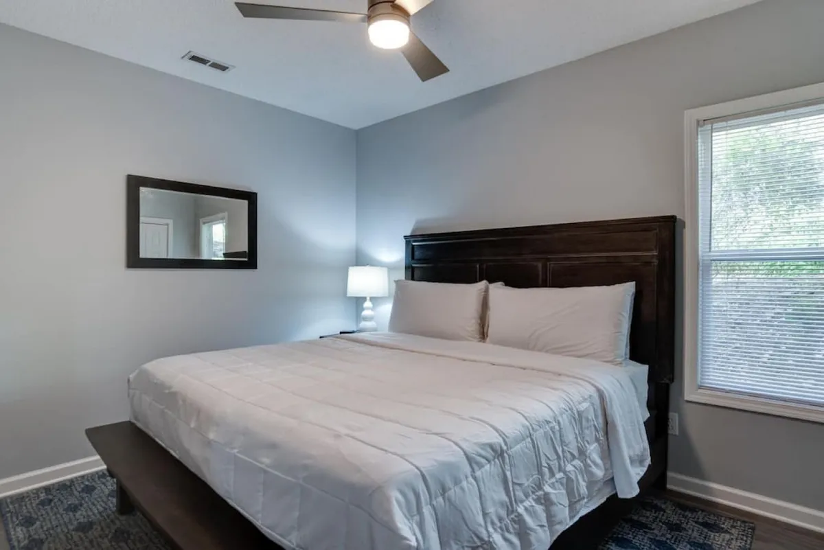 A tranquil bedroom with a bed, mirror, and lamp, set near a window that allows natural light to fill the space. The overall ambiance is quiet, inviting, and restful—perfect for recharging.