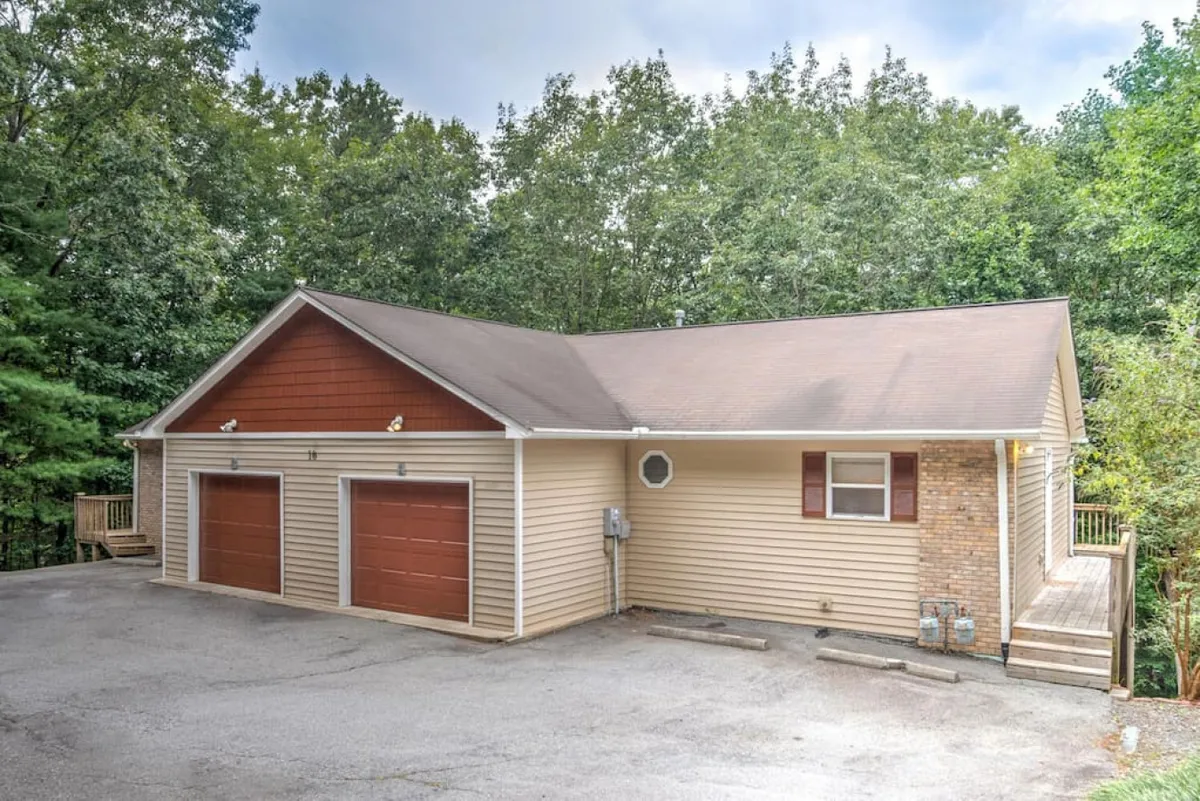 This image shows the exterior of the townhome, featuring two private garage doors, a wooden deck, and attractive brick accents. The scene conveys a sense of secure, convenient parking and a warm, welcoming arrival.