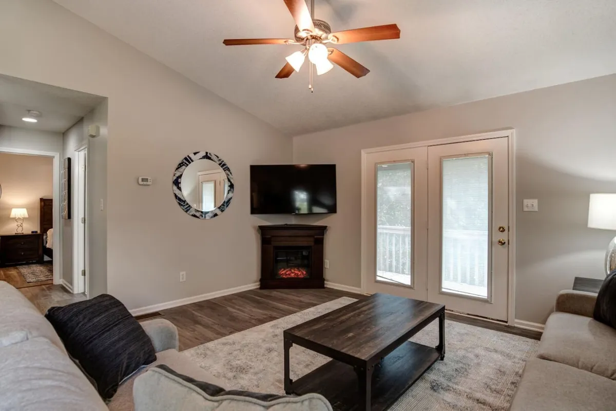 A cozy living room with a plush sofa, coffee table, and a fireplace sits at the heart of this inviting space. Double doors let in abundant natural light and provide a glimpse of the outdoors, suggesting easy access to explore or return from pet-friendly adventures.